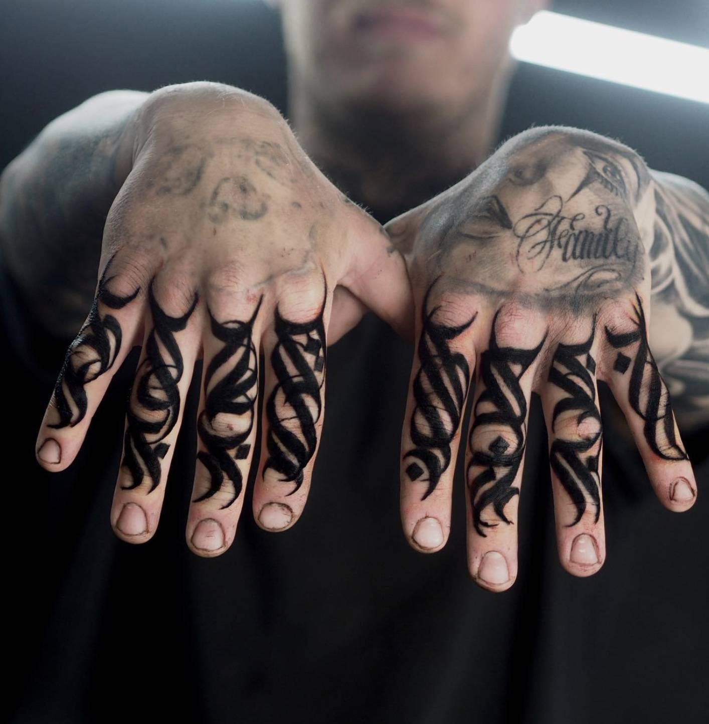 Close-up of two hands with intricate black tribal-inspired tattoos on each finger and hand
